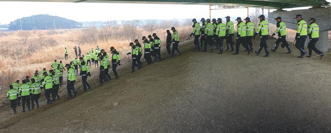황구지천 여정이 끝나갈 즈음, 화성시 향남면 수직리 부근, 강둑으로 기동경찰 대열이 올라선다. 탐침봉과 삽을 들고 갈대숲으로 내려선다. 이미 임무는 받은 듯하다. 한 주일째 행방을 알 수 없는 할머니의 실종사건, 불확실한 단서를 찾아 헤매는 노동의 대열, 강둑에까지 이르렀다. 살아 있길 염원하지만 누워있더라도 존재를 찾아야 한다. 살아서 누워 있다는 것은 평온이지만, 죽어서 누워 있는 것은 절멸의 공포다. 하필 ‘살인의 추억’ 그 쓸쓸한 무대가 화성 땅인가. 트라우마는 길다. 깊다. 퍼 다 버려도 샘솟는다. 경찰, 참 힘든 배역이다.